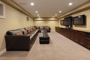 A waterproof basement with a large L-shaped sofa in it, rug and mounted wall TV.